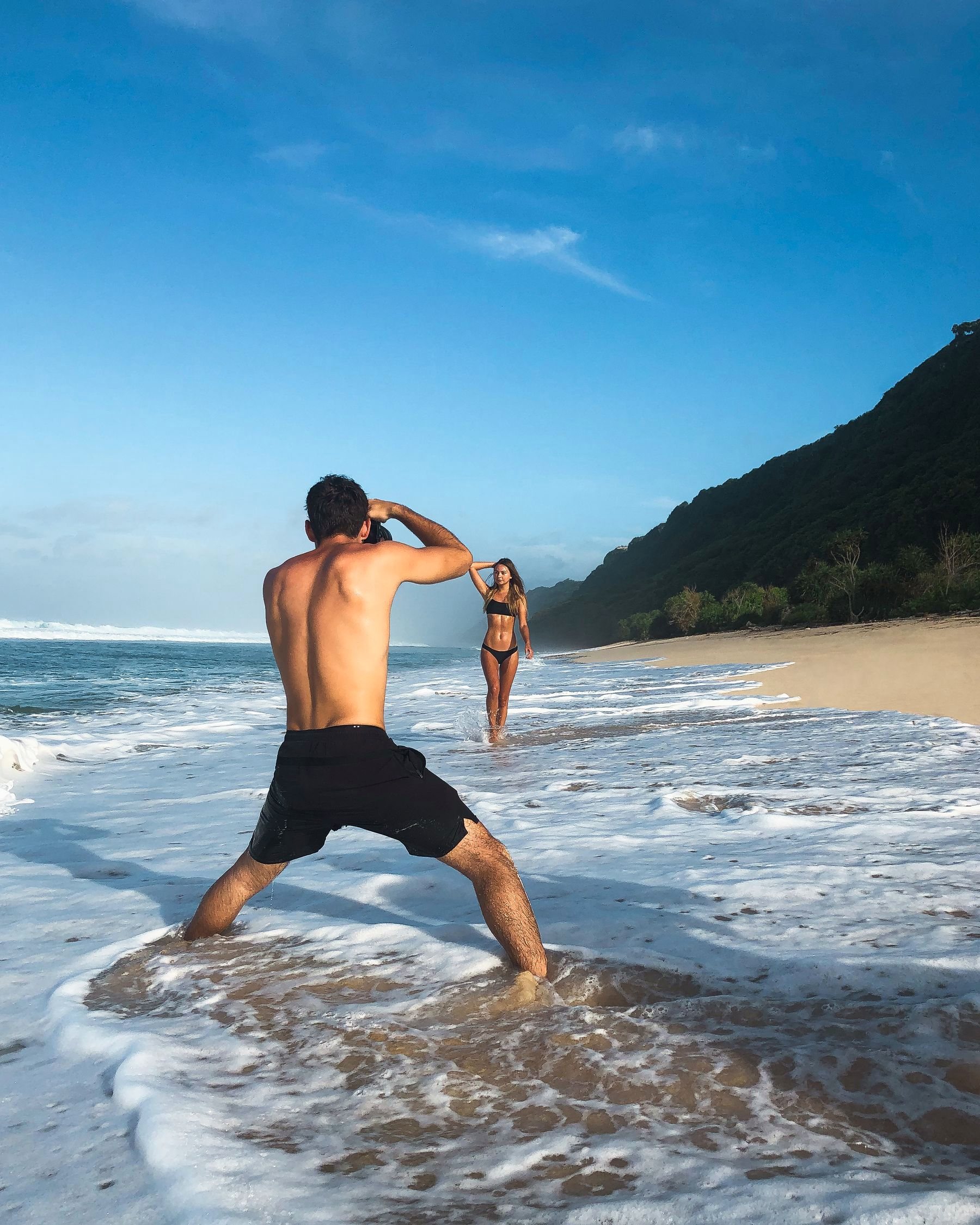 A photographer shooting a model in the surf of a tropical beach